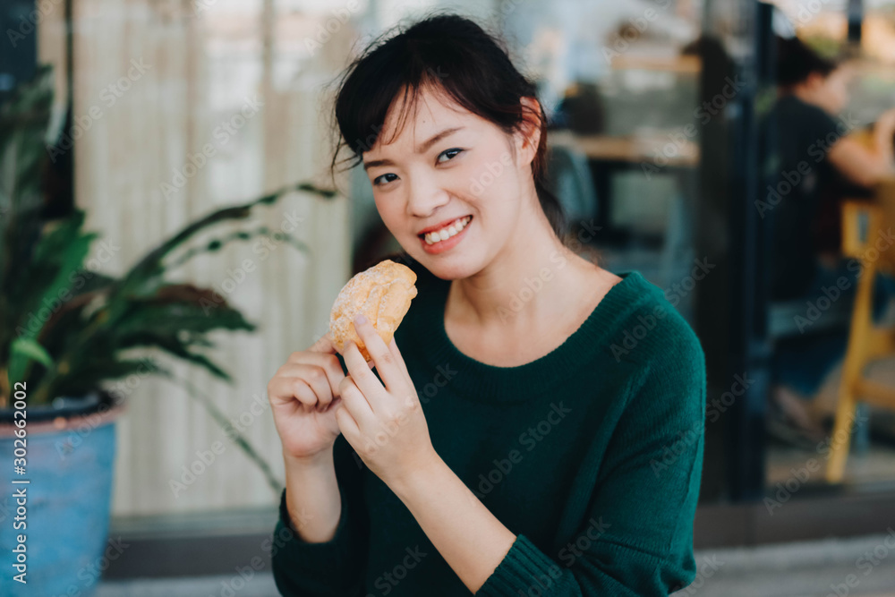 Pretty Asian woman wearing green sweater and enjoyed eating Japanese Puff Cream/Shu cream.