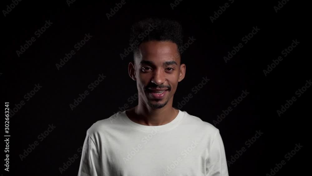 Young african american man in white on black studio background showing yes sign by head. Positive footage, emotions, body language concept. Young african american man in white on black studio background showing yes sign by head. Positive footage, emotions, body language concept.