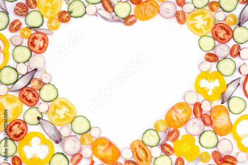 Heart frame made of bright colorful vegetables with copy space. Salad ingredients, tomatoes cucumber peppers onions cut on white, top view, selective focus
