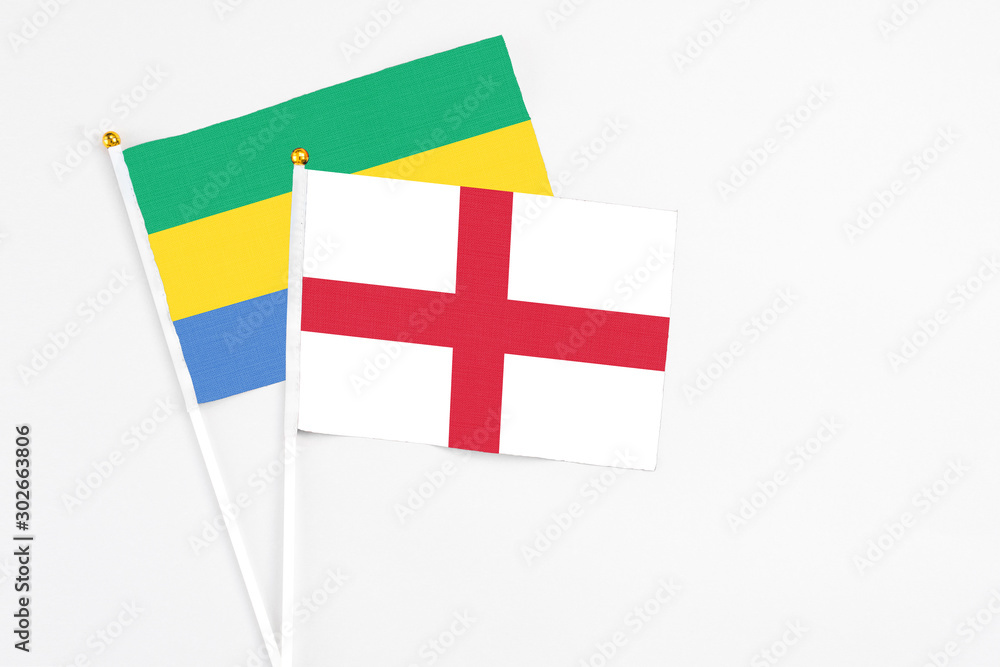England and Gabon stick flags on white background. High quality fabric, miniature national flag. Peaceful global concept.White floor for copy space.