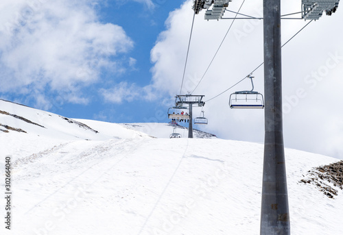 cable car with people in cabins on a mountain slope covered with snow, Caucasus