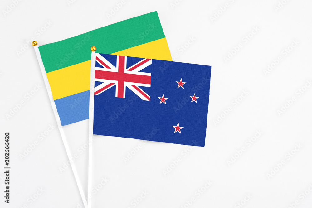 Fototapeta premium New Zealand and Gabon stick flags on white background. High quality fabric, miniature national flag. Peaceful global concept.White floor for copy space.
