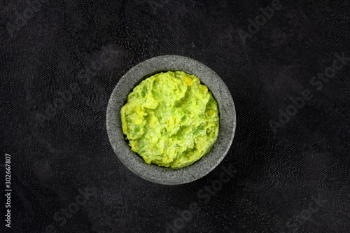 Guacamole in a molcajete, Mexican avocado dip in the traditional stone mortar, shot from the top on a black background photo