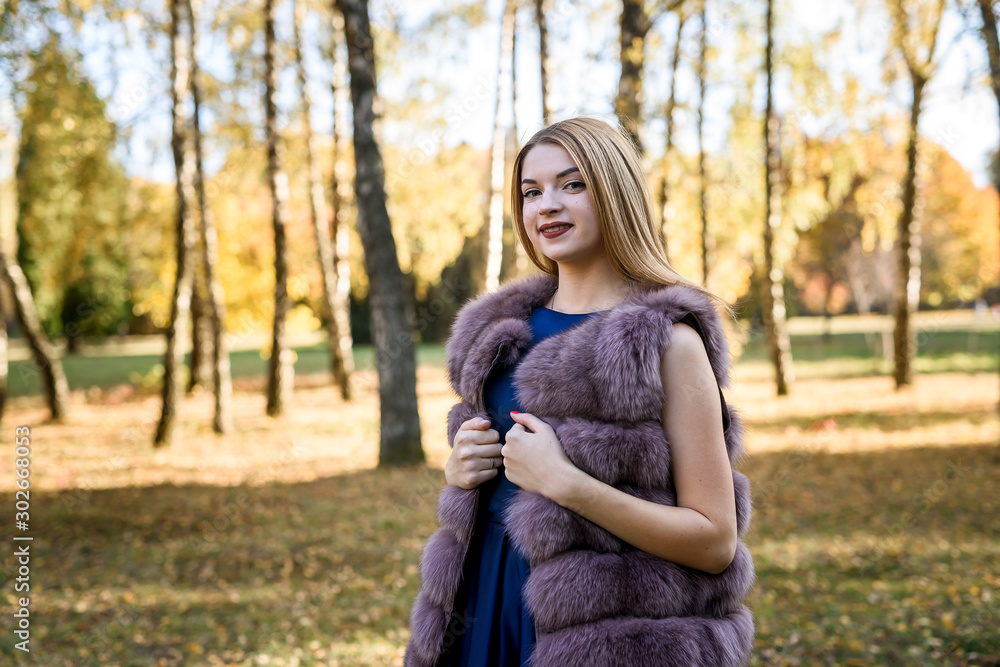 Fashion woman. Smiling girl in fur coat posin in autumn park with trees and ivy Fashion woman. Smiling girl in fur coat posin in autumn park with trees and ivy