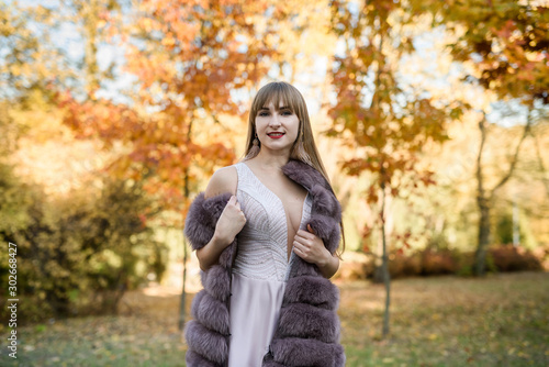 Woman in fashion beige dress and fur coat posing in autumn landscape. Trend clothes