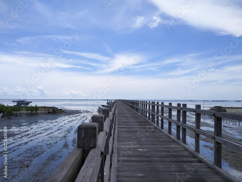 view of a long wooden bridge on the beach with a background of white clouds and beautiful blue sky