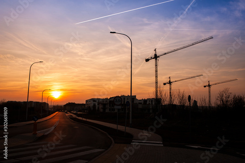 Construction site with building cranes and new built residential buildings. Sunset sky with some clouds.