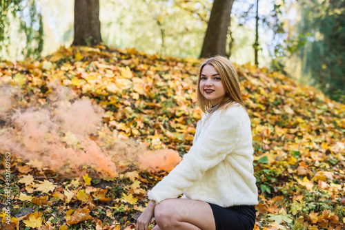 Woman in black dress with smoke bomb in autumn park posing on yellow leaves