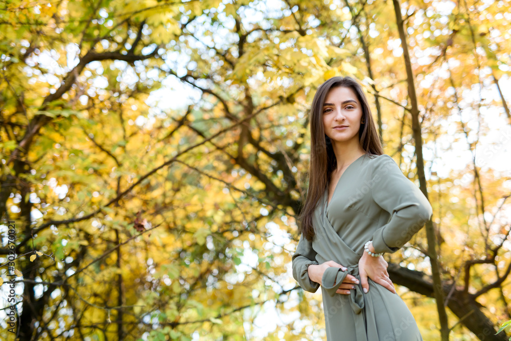 Portrait of brunette woman in green dress posing in autumn park Portrait of brunette woman in green dress posing in autumn park