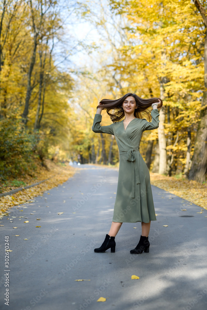 Portrait of brunette woman in green dress posing in autumn park Portrait of brunette woman in green dress posing in autumn park