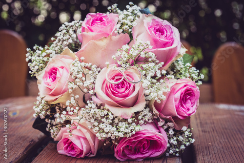 Wedding bouquet with pink roses on wooden table with rings.