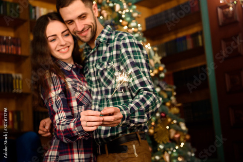 Sparklers and a kiss for Christmas! Young beautiful kisser and burning sparklers. Loving couple in Christmas decorated room.