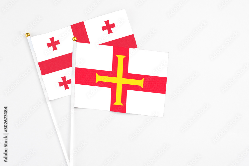 Guernsey and Georgia stick flags on white background. High quality fabric, miniature national flag. Peaceful global concept.White floor for copy space.