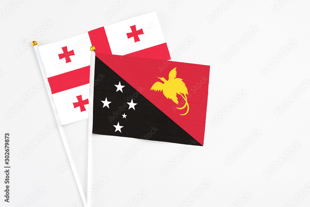 Papua New Guinea and Georgia stick flags on white background. High quality fabric, miniature national flag. Peaceful global concept.White floor for copy space.