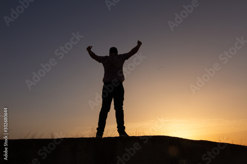 silhouette of man raising arms sunset