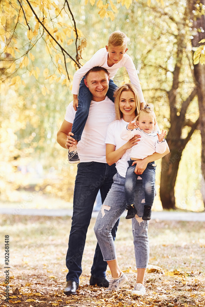 Mother and dad holds kids at shoulders and in hands. Cheerful young family have a walk in an autumn park together Mother and dad holds kids at shoulders and in hands. Cheerful young family have a walk in an autumn park together