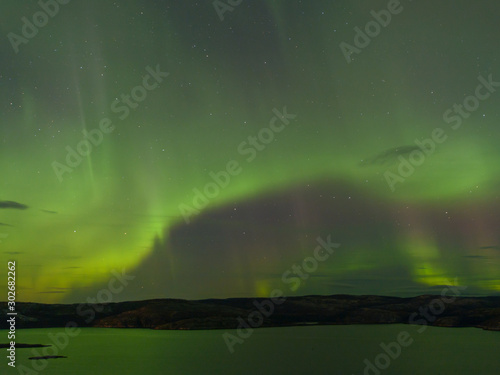 Northern lights over the lake and hills. Aurora at night in the sky in the north. © Moroshka