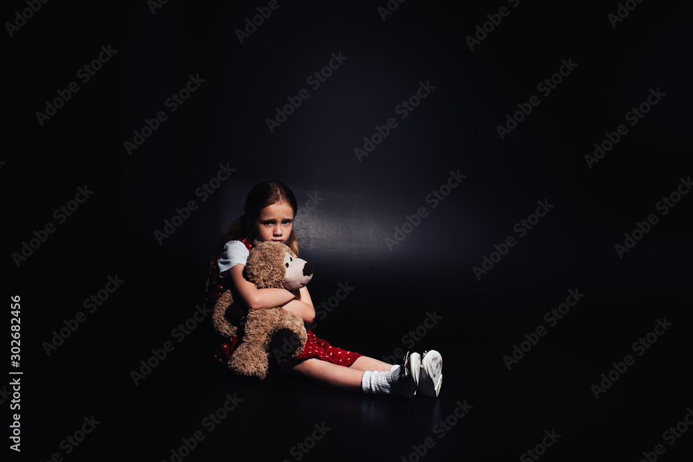 lonely, scared kid sitting on floor and hugging teddy bear on black background lonely, scared kid sitting on floor and hugging teddy bear on black background