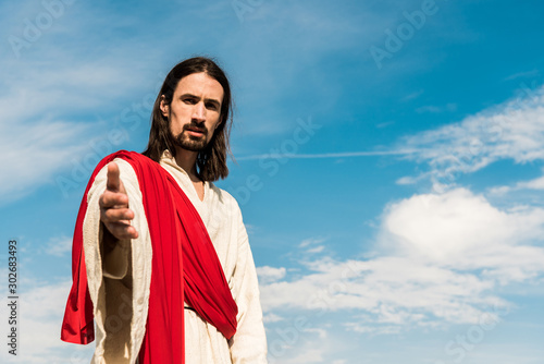 selective focus of jesus gesturing against blue sky with clouds