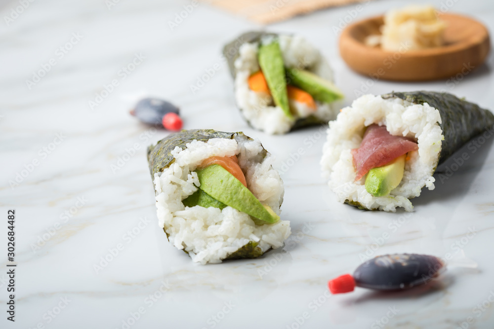 Lachs, Tunfisch und Surimi Avocado Temaki Sushi, eingelegter Ingwer mit Soja Soße Fische und Sushimatte auf Marmor Hintergrund
