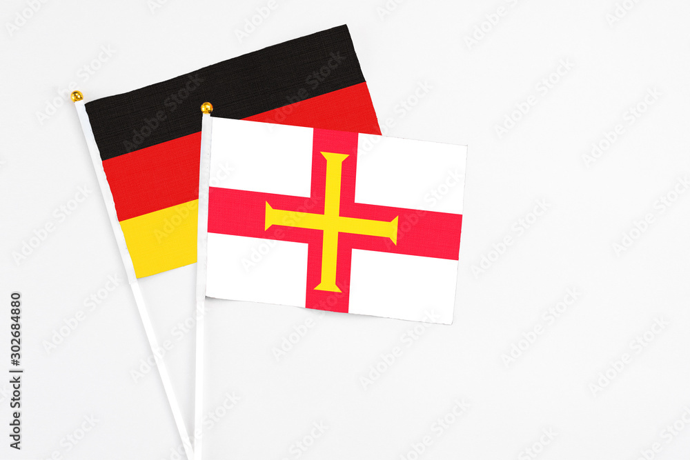 Guernsey and Germany stick flags on white background. High quality fabric, miniature national flag. Peaceful global concept.White floor for copy space.