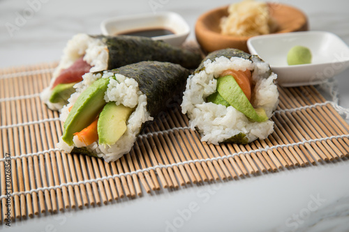 Lachs Fisch, Tunfisch und Surimi Avocado Temaki Sushi, eingelegter Ingwer mit Soja Soße und Sushimatte auf Marmor Hintergrund