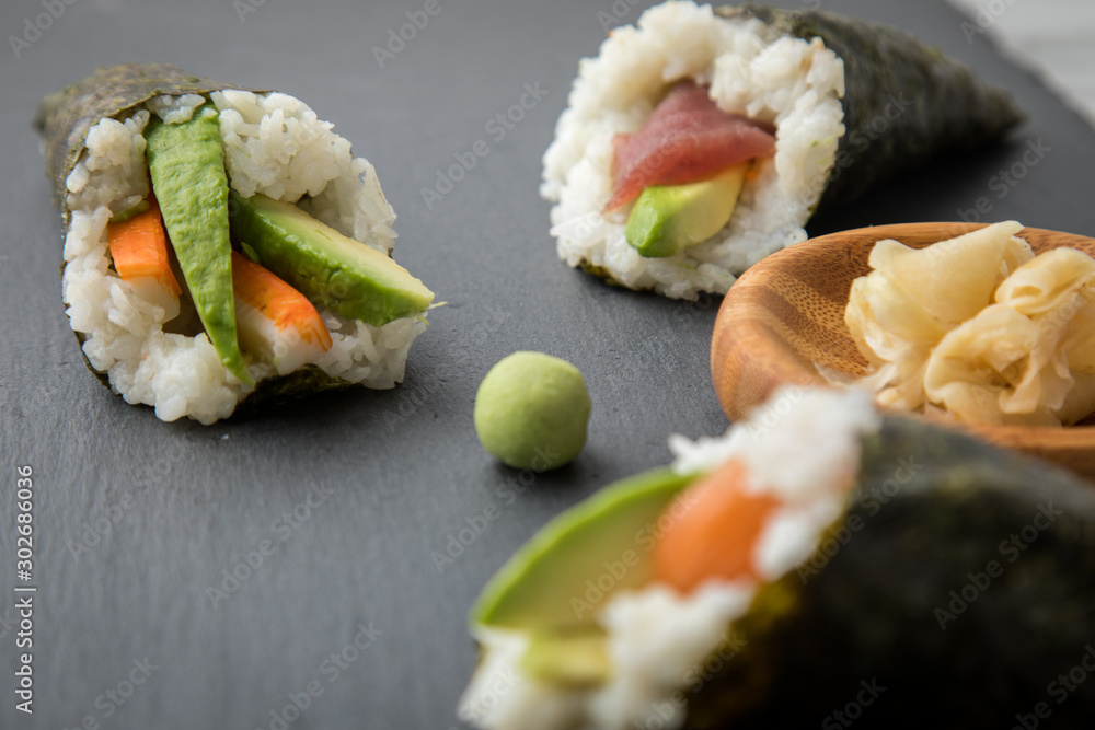 Lachs Fisch, Tunfisch und Surimi Avocado Temaki Sushi, eingelegter Ingwer und Wasabi auf Schiefer Platte und Marmor Hintergrund Lachs Fisch, Tunfisch und Surimi Avocado Temaki Sushi, eingelegter Ingwer und Wasabi auf Schiefer Platte und Marmor Hintergrund