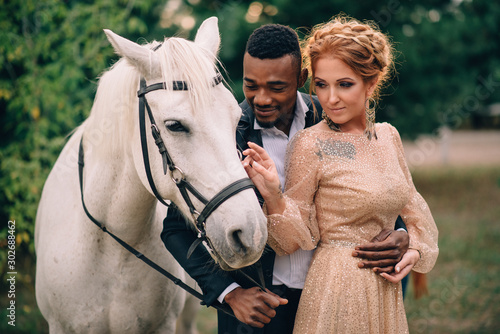 Newlyweds are standing near a white horse in nature