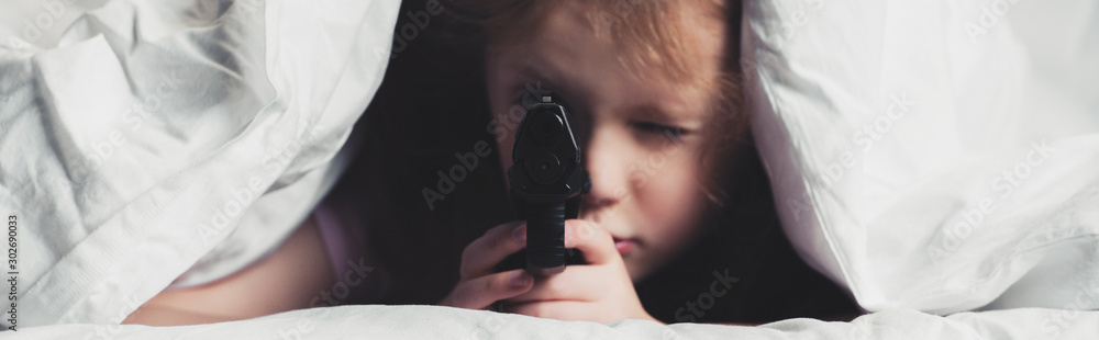 panoramic shot of scared child holding gun while hiding under blanket panoramic shot of scared child holding gun while hiding under blanket