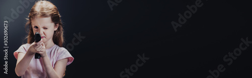 panoramic shot of kid holding pistol while looking at camera on black background