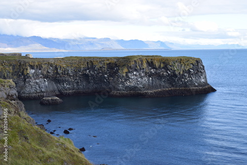 Green cliff overlooking the water in Iceland. Beautiful scenery on a cloudy day. Icelandic landscape.