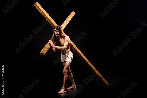 shirtless jesus in wreath holding wooden cross and walking on black photo