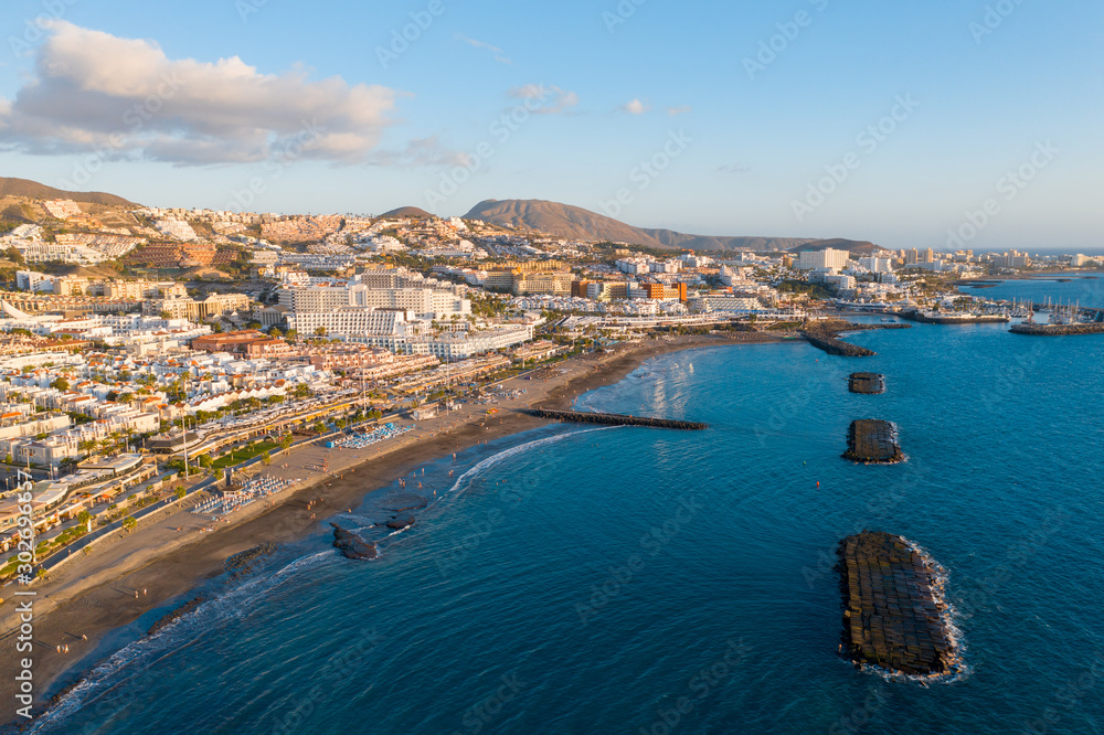 Drone aerial shot of Costa Adeje area, South Tenerife, Spain. Captured at golden hour, warm and vivid sunset colors. Luxury hotels, villas and restaurants behind the beach.