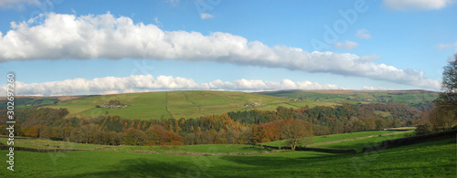 wide panoramic view of west yorkshire countryside with the forest of hardcastle crags in the bottom of a wide valley surrounded by meadows with grazing sheep in bright autumn sunshine