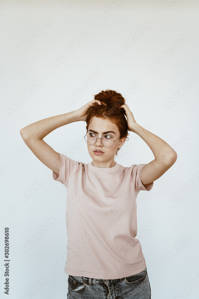 a young student strictly looks through the glasses sideways and straightens her hair. light background a young student strictly looks through the glasses sideways and straightens her hair. light background