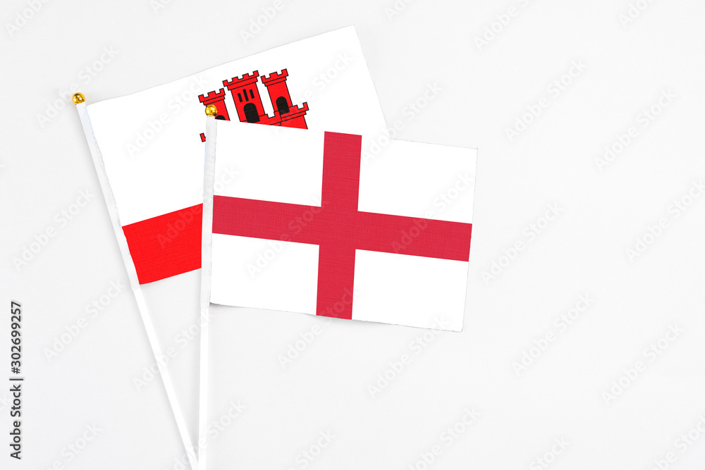 England and Gibraltar stick flags on white background. High quality fabric, miniature national flag. Peaceful global concept.White floor for copy space.