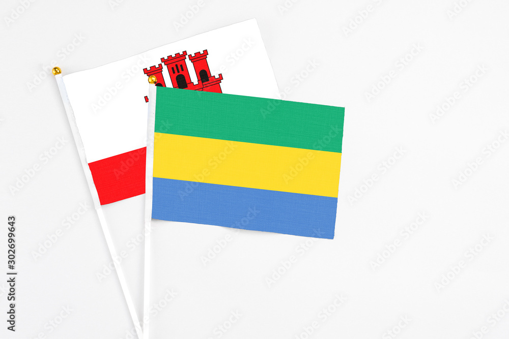 Gabon and Gibraltar stick flags on white background. High quality fabric, miniature national flag. Peaceful global concept.White floor for copy space. Gabon and Gibraltar stick flags on white background. High quality fabric, miniature national flag. Peaceful global concept.White floor for copy space.