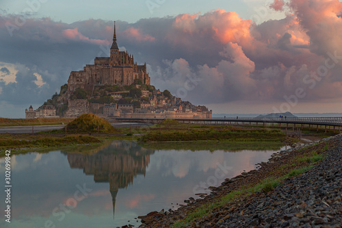 Normandy, France. Le Mont Saint Michel with a large red cloud is reflected in the sea during sunrise.