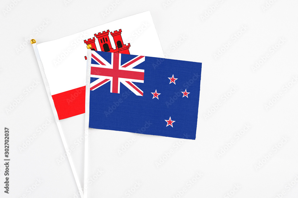Fototapeta premium New Zealand and Gibraltar stick flags on white background. High quality fabric, miniature national flag. Peaceful global concept.White floor for copy space.