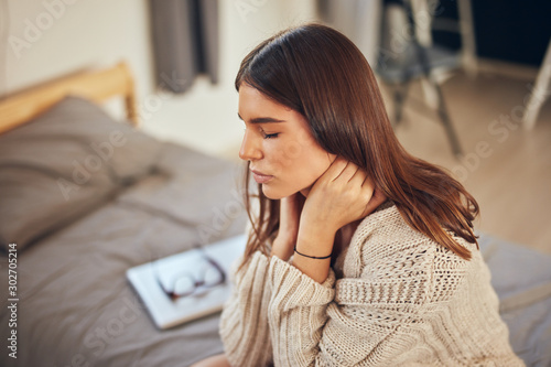 Attractive caucasian brunette having neck pain. Bedroom interior.