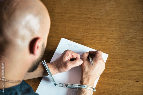 Men hands with handcuffs fill the police record, confession. on top of the police investigative detective. Arrest, bail, criminal, prison. fingerprints, criminal. photo