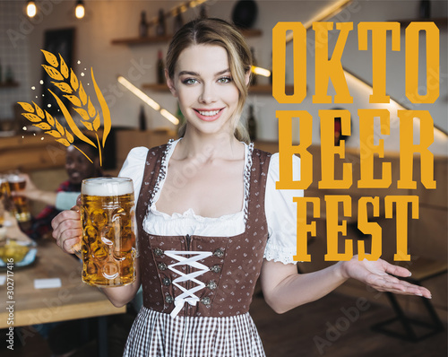 attractive waitress in german national costume holding mug of light beer and looking at camera near Oktobeerfest illustration photo