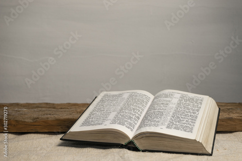Fotografia, Obraz Open Holy Bible on a old wooden table and white wall background