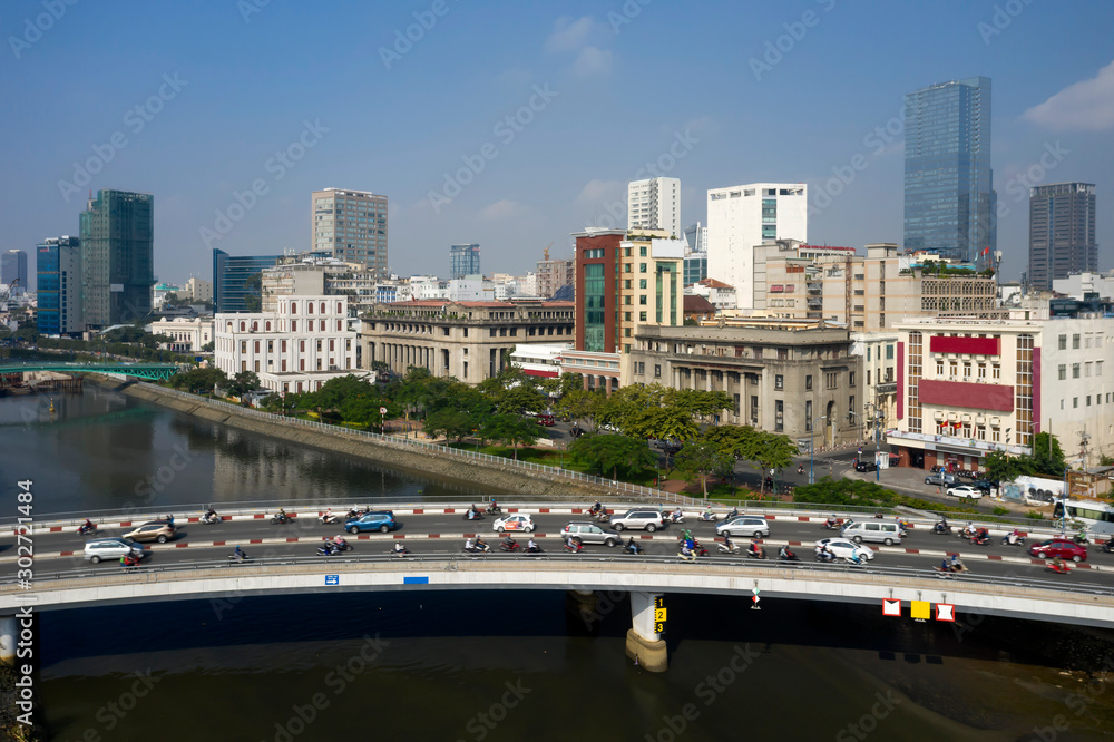 Wide Drone shot of Morning traffic on Khanh Hoi Bridge over Ben Nghe Canal separating districts four and one in Ho Chi Minh City. Background features financial and banking district