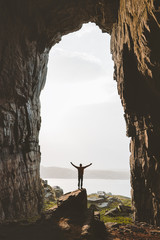 Man standing alone in cave Travel adventure vacations happy raised hands tourist success wellness concept Kirkehelleren grotto in Norway