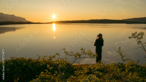 Midnightsun w Skandynawii. Dziewczyna łowi ryby przed wspaniałą scenerią. Czapka na komary jest koniecznością.