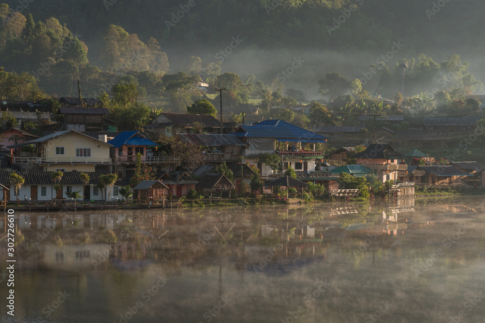 Fototapeta premium Morning view of Ban Rak Thai Village,Chinese Yunnan village on lakeside with fog,sunlight and green hill background, Ban Rak Thai,Mae Hong Son, northern of Thailand