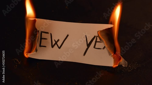 New Year word written on white paper burns. Fire with smoke and ashes on black background photo