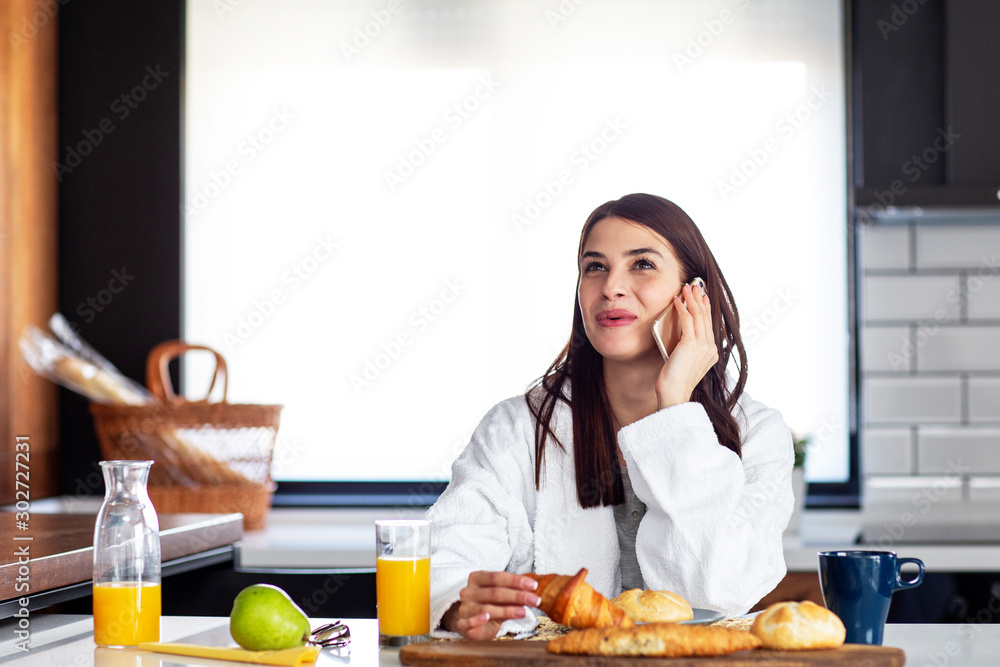 With breakfast at the kitchne with pastry and orange juice on table young woman start in the morning using mobile phone