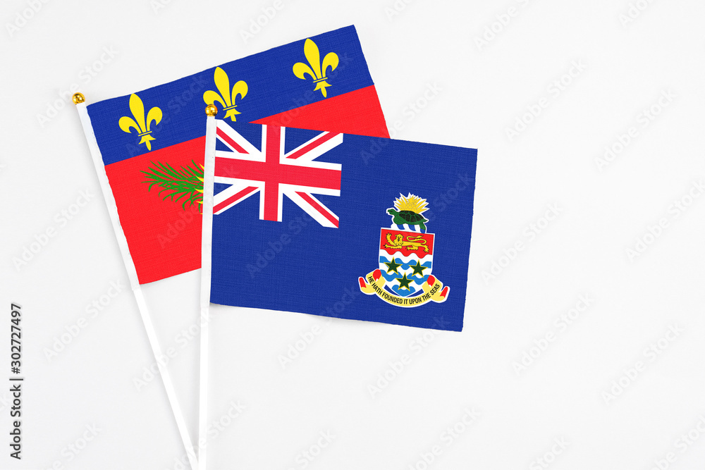 Fototapeta premium Cayman Islands and Guadeloupe stick flags on white background. High quality fabric, miniature national flag. Peaceful global concept.White floor for copy space.